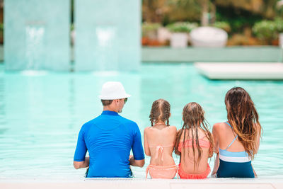 Rear view of family sitting by swimming pool