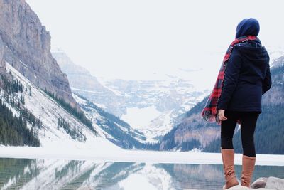 Full length rear view of woman standing by lake against snowcapped mountains