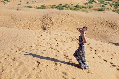 Brunette woman in a long leopard dress stands with her back in the desert at sunset. go everywhere