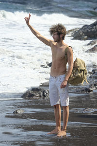 Full length of shirtless man with backpack standing at beach