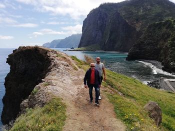 Senior man walking with son on cliff against sea