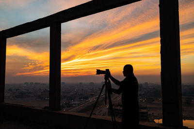 Silhouette woman photographing against sky during sunset