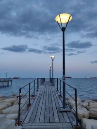 Street lights on pier by sea against sky