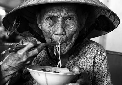 Close-up portrait of senior woman eating noodles while sitting at home