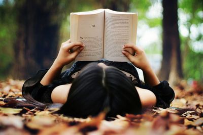 Woman reading book while lying on field 