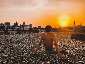 Man sitting on beach against buildings in city during sunset