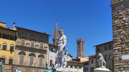 Low angle view of statue and historic buildings against clear blue sky