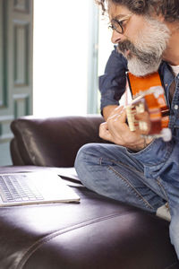 Bearded man learns to play acoustic guitar online from home