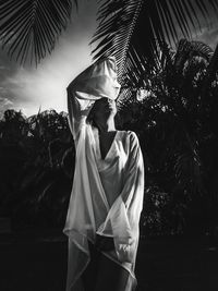 Woman covering eyes while standing by palm trees