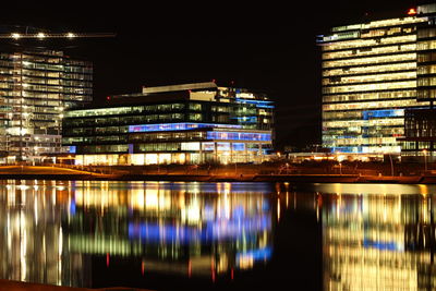 Illuminated modern buildings by river at night