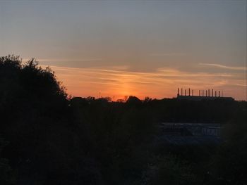 Silhouette trees and cityscape against sky during sunset