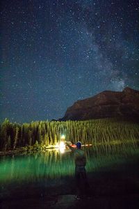 Man standing on illuminated mountain against star field at night