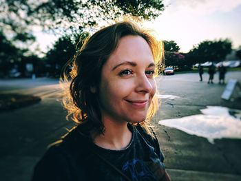 Close-up of smiling young woman looking away while standing on street during sunset