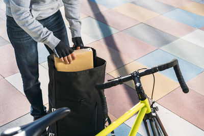 Delivery man removing package from backpack by bicycle on footpath