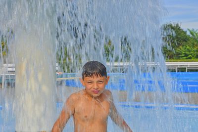 Little boy in the small swimming pool. boy taking shower in water park. boy standing under sprinkler