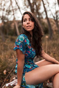 Side view of woman sitting on land in forest