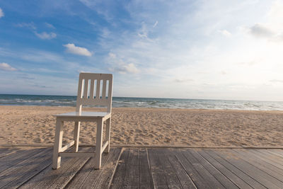 Chair on floorboard at beach against sky