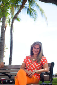 Portrait of smiling woman sitting on bench at park