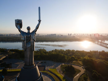 Man standing on bridge over cityscape against sky during sunset