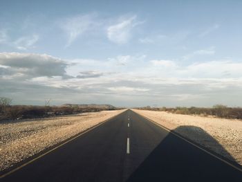 Road passing through field against sky