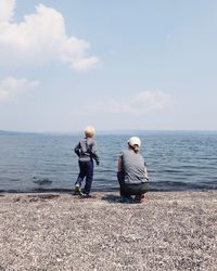 Rear view of mother with son at beach against sky