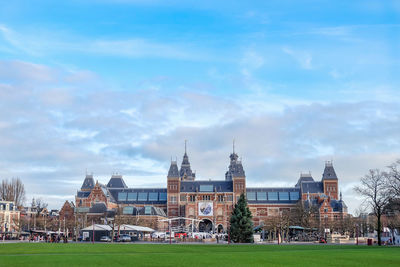 Grassy field by historic building in city against sky