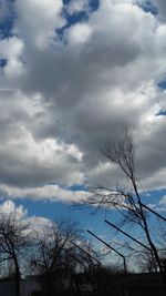 Low angle view of bare trees against cloudy sky