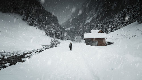 Rear view of woman walking on field against mountains during snowfall