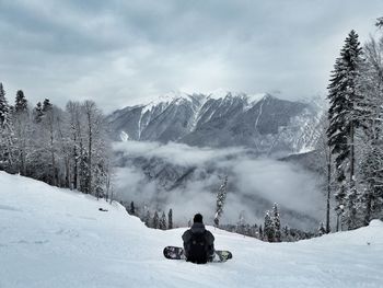 Rear view of man sitting on snow covered landscape