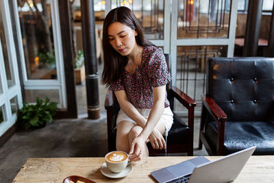 Young woman using mobile phone while sitting on table