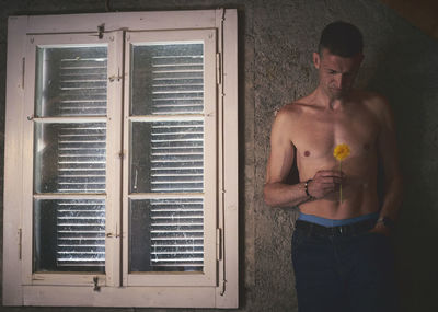 Full length of shirtless man standing by window