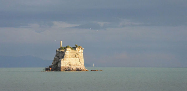 Lighthouse on sea by building against sky