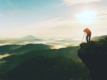 Nature photographer in the action. man silhouette above a misty clouds, morning hilly landscape.