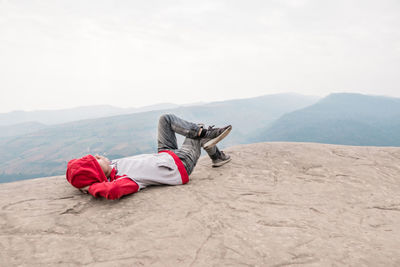 Man lying on rock against sky