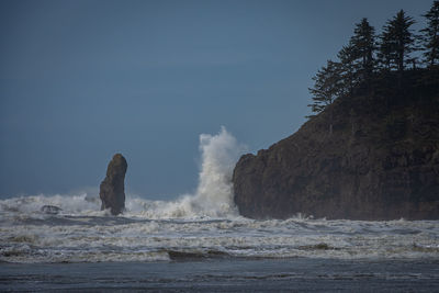 Sea waves splashing on rocks against sky