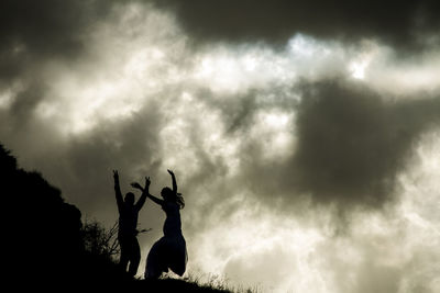 Low angle view of silhouette women standing against cloudy sky