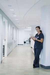 Portrait of female doctor using tablet computer while leaning against architectural column in hospital