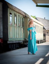 Side view of young woman wearing blue dress while walking on railroad station platform