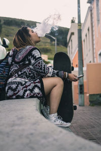 Young woman smoking cigarette while sitting outdoors