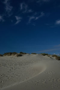 Footprints on sand dune in desert against blue sky