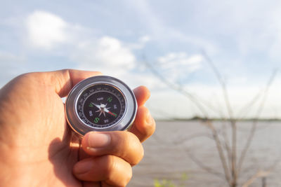 Cropped hand holding navigational compass against sea