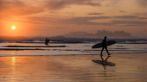 Silhouette people at beach against sky during sunset