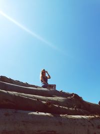 Low angle view of woman sitting on wood against clear sky