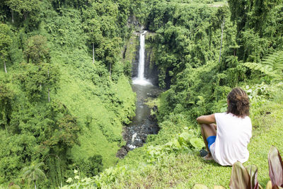 Male tourist with curly hair, looking at exotic fuipsia waterfall