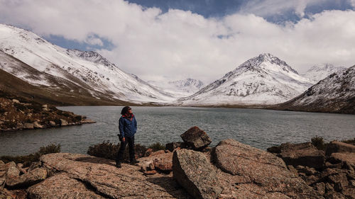 Man standing on rock by lake against sky