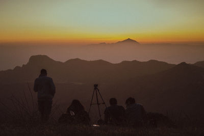 Rear view of silhouette people photographing mountains against sky during sunset