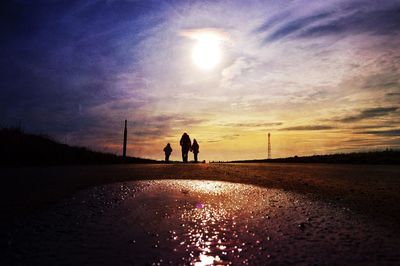 Silhouette men on road against sky during sunset