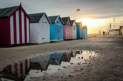 Beach huts by buildings against sky during sunset