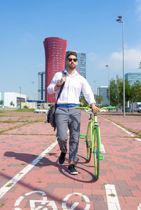 Bearded man in sunglasses walking with bike by bicycle track outdoors