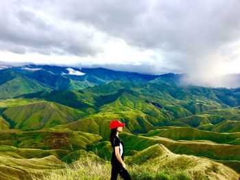 Side view of female hiker standing on mountain against cloudy sky